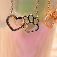 Load image into Gallery viewer, Gold tone and silver tone necklaces with open heart charms intertwined with open pet paw charms. Displayed hanging from irridescent cup.