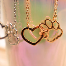 Load image into Gallery viewer, Gold tone and silver tone necklaces with open heart charms intertwined with open pet paw charms. Displayed hanging from irridescent cup.