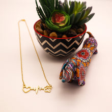 Load image into Gallery viewer, Gold tone necklace with open heart, heartbeat rhythm, and open pet paw. Displayed beside succulent plant with a cute mosaic dachsund figurine.