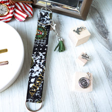 Load image into Gallery viewer, closeup picture of an Army Charmable Wristlet keychain on a white wood with other elements in the background and three charms on small light wood blocks.