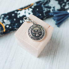 Load image into Gallery viewer, Closeup of the Navy Seal charm on a light wood block with a Navy Charmable keychain in the background.