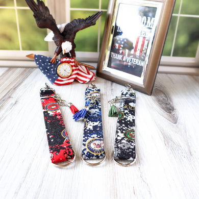Picture of Marine, Navy and Army Charmable Wristlet keychain.  Displayed on a white board with a window in the background, an eagle clock and a picture thanking veterans. 