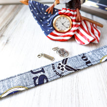 Load image into Gallery viewer, Closeup of an Air Force Motto Charmable Wristlet keychain on white wood with an eagle clock and two charms in the background (Brave and Air Force seal).