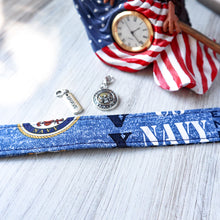Load image into Gallery viewer, closeup of a Navy Motto pattern Charmable Wristlet keychain on white wood with an eagle clock and two charms in the background (Brave and Navy Seal).