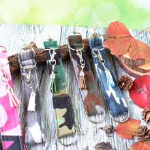 Load image into Gallery viewer, Close up of the pink, gray, green, brown and blue camo patterns of Charmable Wristlet keychains. Displayed on a wood with a branch, orange leaves and pine cones.