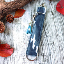 Load image into Gallery viewer, Close up of the blue camo Charmable Wristlet Keychain. Displayed on a wood with a branch, orange leaves and pine cones.