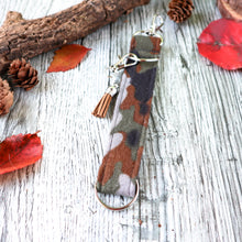 Load image into Gallery viewer, Closeup of the brown camo Charmable Wristlet keychain. Displayed on a wood with a branch, orange leaves and pine cones.