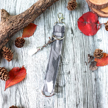 Load image into Gallery viewer, Closeup of the gray camo Charmables Wristlet Keychain. Displayed on a wood with a branch, orange leaves and pine cones.