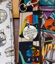Load image into Gallery viewer, A picture of a silver round charm with the outline of Yoday and the words "May the Force Be With You." Charm has a lobster clasp and is displayed on a collection of Charmable wristlet keychains.