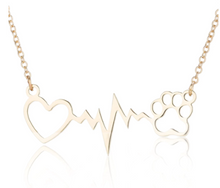 Load image into Gallery viewer, Gold tone necklace with open heart and paws connected by a heartbeat rhythm. Diplayed on white background.