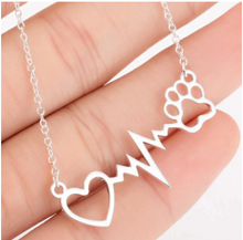 Load image into Gallery viewer, Silver necklace with open heart, heartbeat rhythm, and open pet paw. Displayed on open hand.