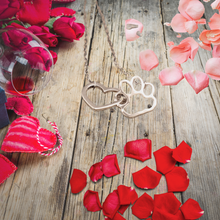 Load image into Gallery viewer, Silver tone necklace with open heart charms intertwined with open pet paw charms. Displayed on background with wood, roses, and flower petals.