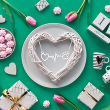 Load image into Gallery viewer, Silver tone necklace with open heart and paws connected by a heartbeat rhythm. Diplayed on teal colored background with flowers, mugs, and a woven heart wreath.