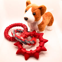 Load image into Gallery viewer, Side view picture of Dogzilla Dino Links dog toy. Toy has two hard red rubber rings connected by a twisted red/light gray/dark gray rope ring. One hard rubber ring has ridges for texture. The second rubber ring has pointed spikes. Displayed on a white background. with a stuffed corgi toy.
