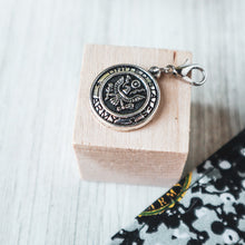 Load image into Gallery viewer, Picture of an Army Seal charm on a small light wood block on a white wood platform with a corner of an Army Charmable Wristlet keychain.
