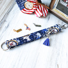 Load image into Gallery viewer, Picture of a Navy Charmable Wristlet keychain on white wood with an eagle clock, corner of a picture and three charms.
