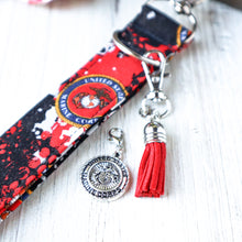 Load image into Gallery viewer, closeup picture of a Marine Charmable Wristlet keychain with a red tassel on white wood and a Marine Seal charm. 
