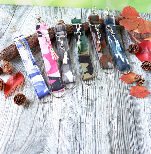 Picture of the six camo color patterns of Charmables Wristlet Keychains.  Displayed on a wood with a branch, orange leaves and pine cones. 