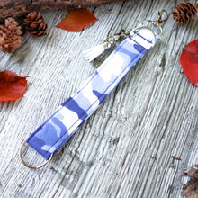Load image into Gallery viewer, Close up of the periwinkle camo Charmables Wristlet keychain. Displayed on a wood with a branch, orange leaves and pine cones.
