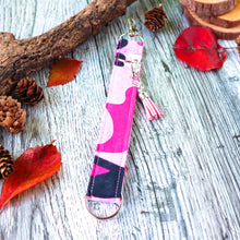 Load image into Gallery viewer, Close up of the pink camo Charmables Wristlet keychain. Displayed on a wood with a branch, orange leaves and pine cones.
